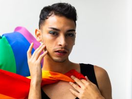 Portrait of biracial transgender man holding rainbow flag on white background. Gender, lgbtq, pride and lifestyle, unaltered.