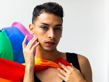 Portrait of biracial transgender man holding rainbow flag on white background. Gender, lgbtq, pride and lifestyle, unaltered.