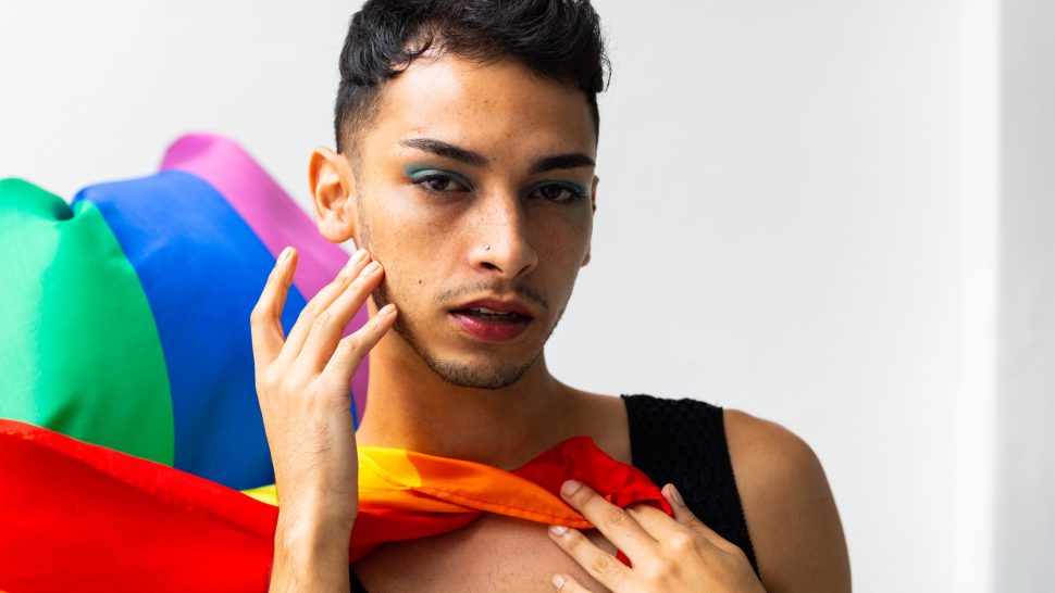 Portrait of biracial transgender man holding rainbow flag on white background. Gender, lgbtq, pride and lifestyle, unaltered.