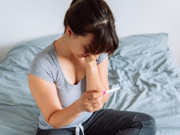 young pretty woman holding pregnancy test with unhappy view