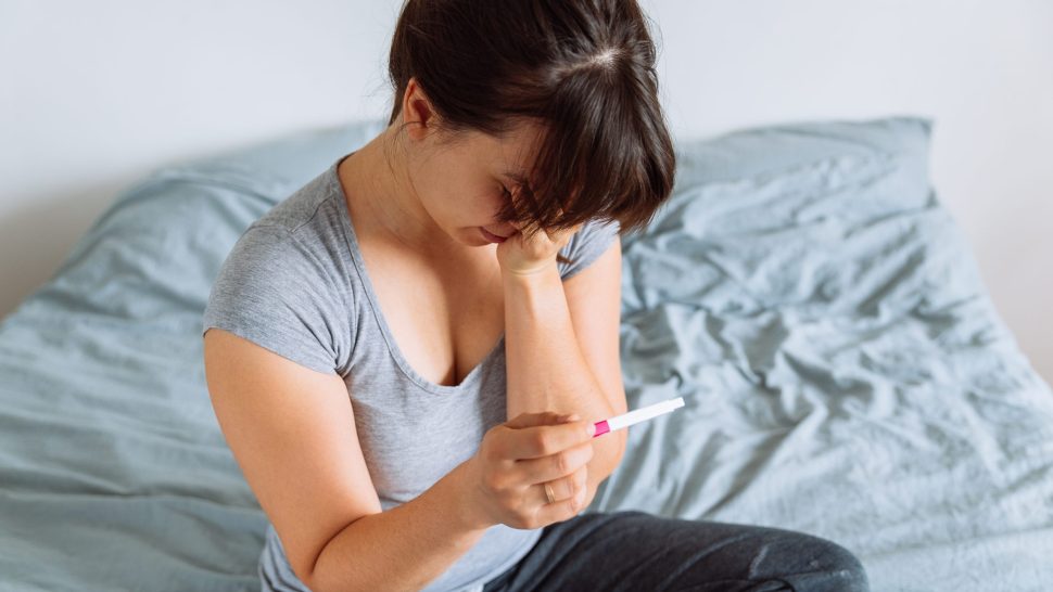 young pretty woman holding pregnancy test with unhappy view