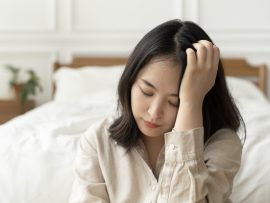 Asian woman sitting sad by her bed