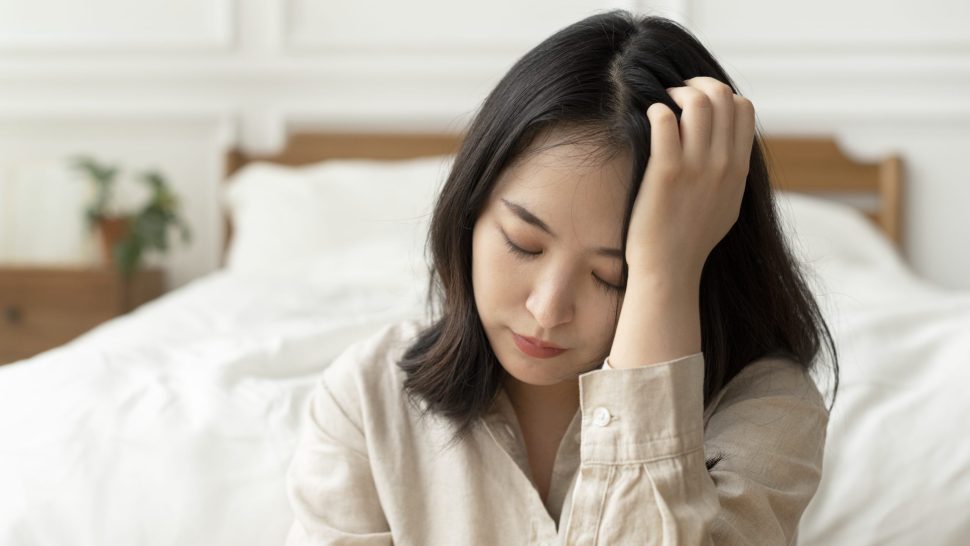 Asian woman sitting sad by her bed