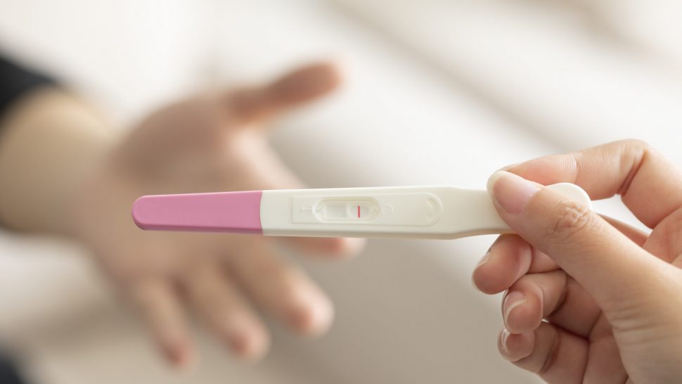 A closeup of a woman's hand holding up a pregnancy test kit with a negative result