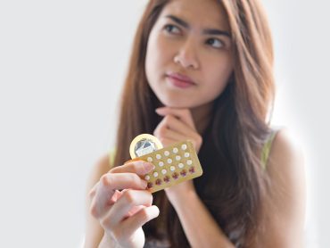 Young woman holding condom and contraceptive pills prevent pregnancy