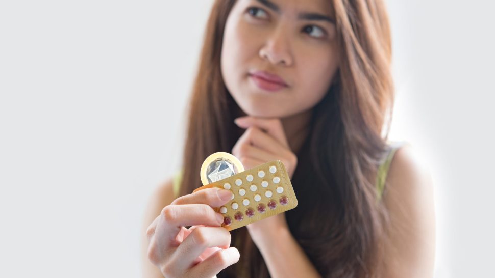 Young woman holding condom and contraceptive pills prevent pregnancy