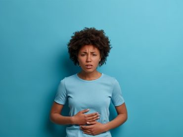 displeased-afro-woman-feels-discomfort-stomach-keeps-palms-tummy-has-period-cramps-wears-casual-t-shirt-ate-spoiled-food-isolated-blue-wall-expresses-negative-emotions-with-mimic_273609-38321