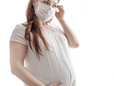 The expectant mother in a white T-shirt with a protective mask against the coronavirus on her face.