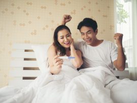 Happy couple smiling after find out positive pregnancy test in bedroom