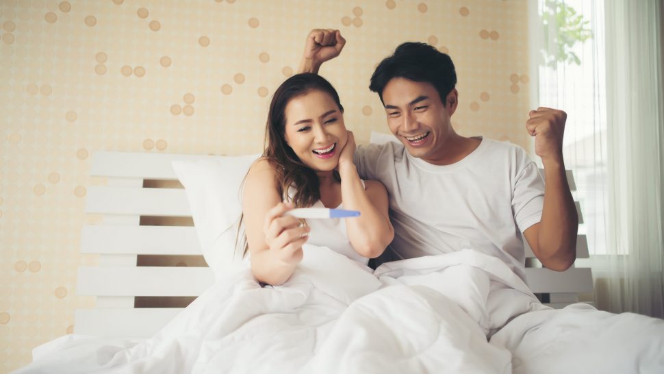 Happy couple smiling after find out positive pregnancy test in bedroom