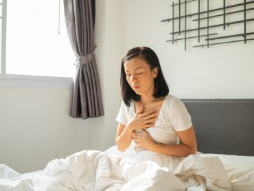 Morning sickness. Young pregnant woman sitting on bed, covering her mouth feeling nauseous during pregnancy, Woman in white pajamas suffering from Acid reflux while wake up on her bed in the morning.
