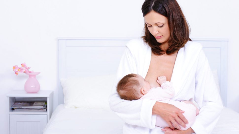 Young mother feeding her little baby with breast at home - indoors