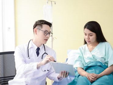 Asian male doctors use a stethoscope to check the heart rhythm of a female patient lying in a hospital bed. Concepts of health examination and medical services