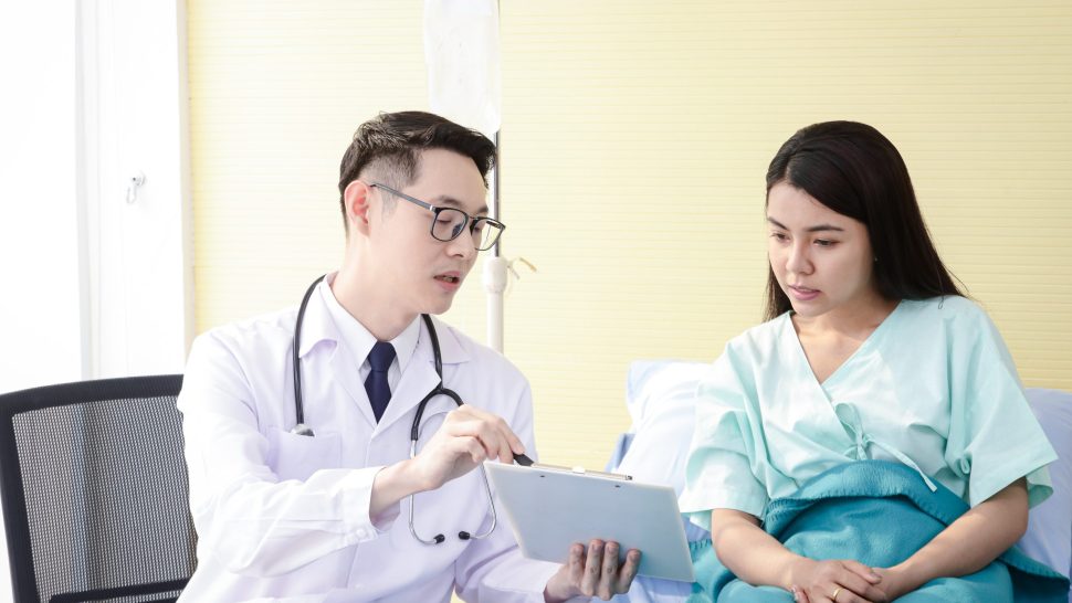Asian male doctors use a stethoscope to check the heart rhythm of a female patient lying in a hospital bed. Concepts of health examination and medical services
