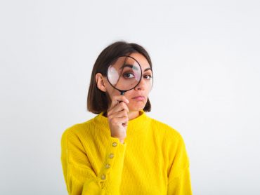 Pretty woman in yellow sweater on white background held magnifier happy positive playful