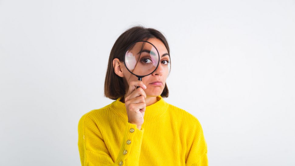 Pretty woman in yellow sweater on white background held magnifier happy positive playful