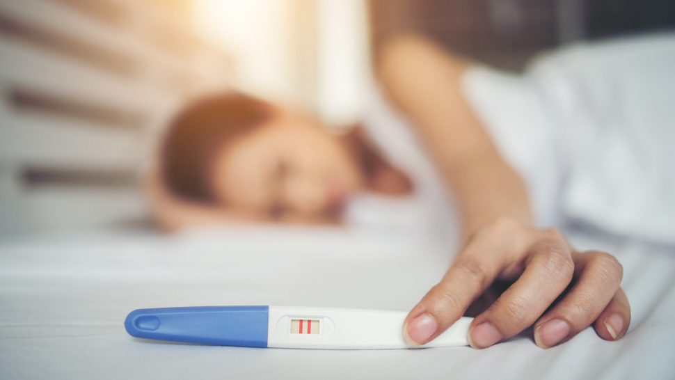 Sad woman complaining holding a pregnancy test sitting on bed