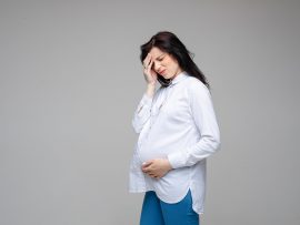 sick caucasian pregnant female touches her head because of a strong headache