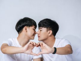 Two loving young men look at each other and make a hand of love symbol.